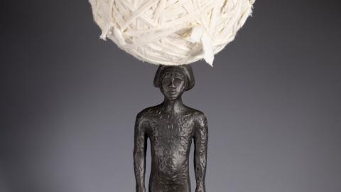 Bronze female figure with large ball of white cotton balanced on her head.